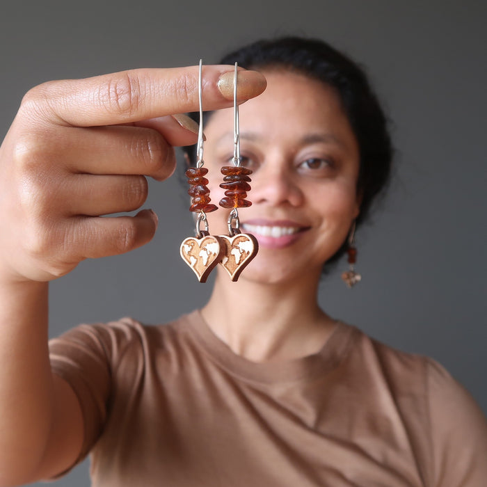 sheila holding large sterling silver earring wires beaded with amber nugget beads and dangling with wood heart world map charms