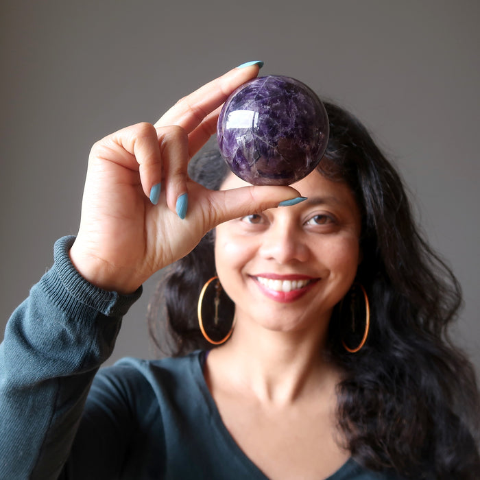 sheila of satin crystals holding up an amethyst sphere at the third eye chakra