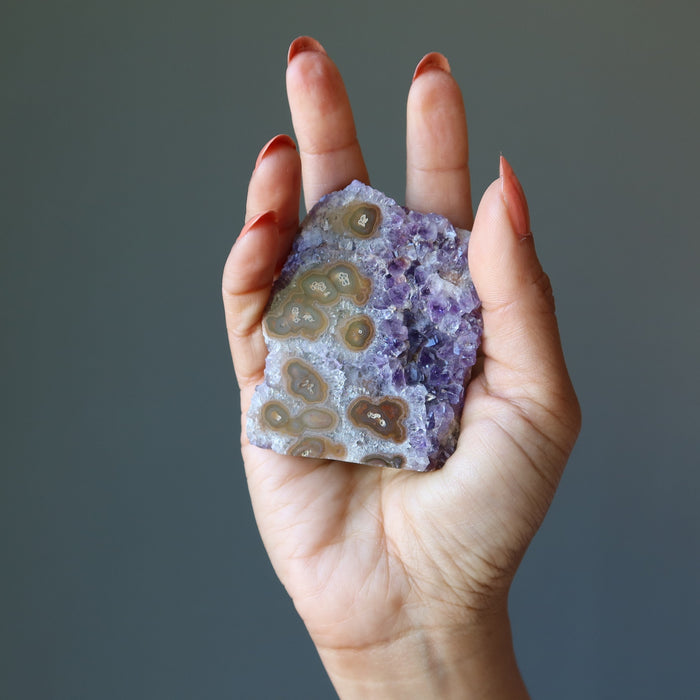 hand holding amethyst cluster with many brown banded eyes