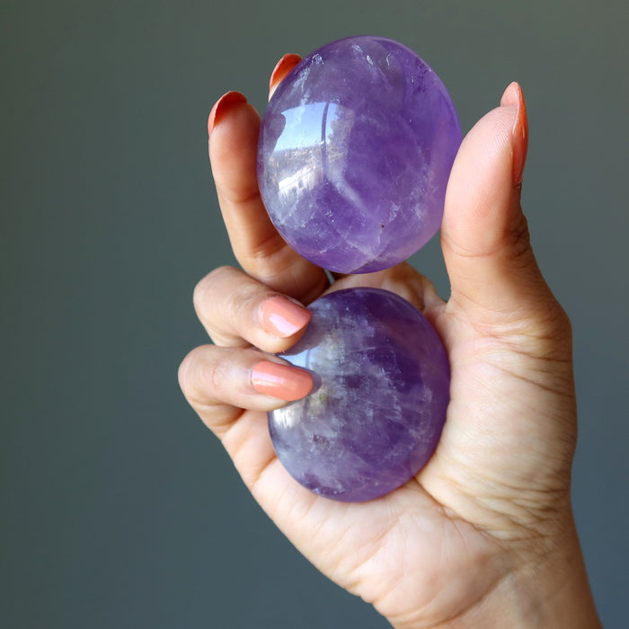 hand holding pair of purple amethyst polished ovalish palm stones