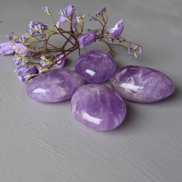 4 purple amethyst polished ovalish palm stones with purple flowers behind
