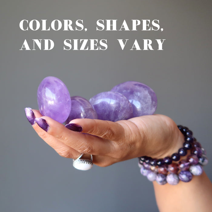 four purple amethyst polished ovalish palm stones in hand showing colors, shapes and sizes vary