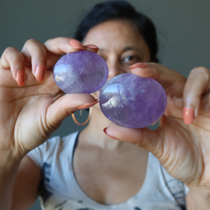 hand holding two purple amethyst polished palm stones of different sizes