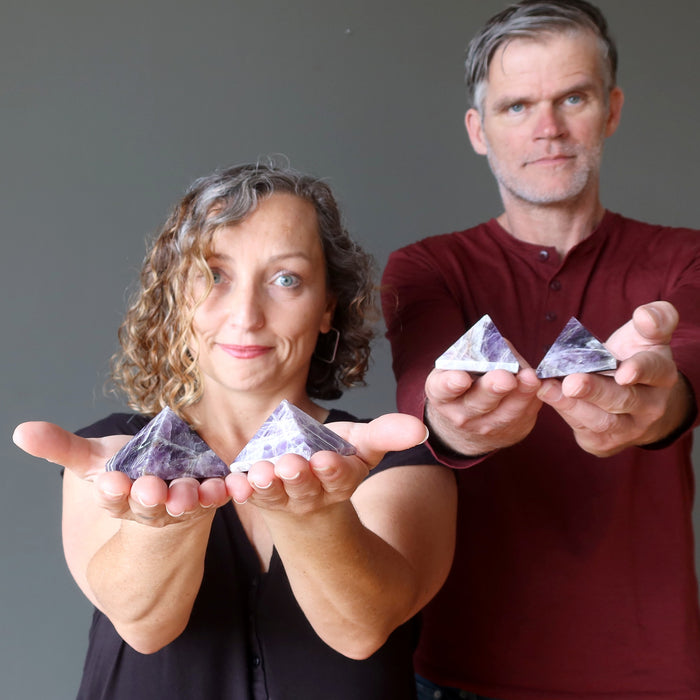 man and woman holding amethyst pyramids
