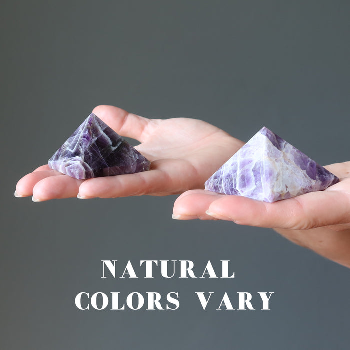hands holding two amethyst pyramids to show natural colors vary