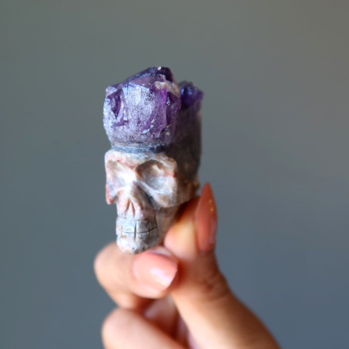 hand holding skull carved from an amethyst geode