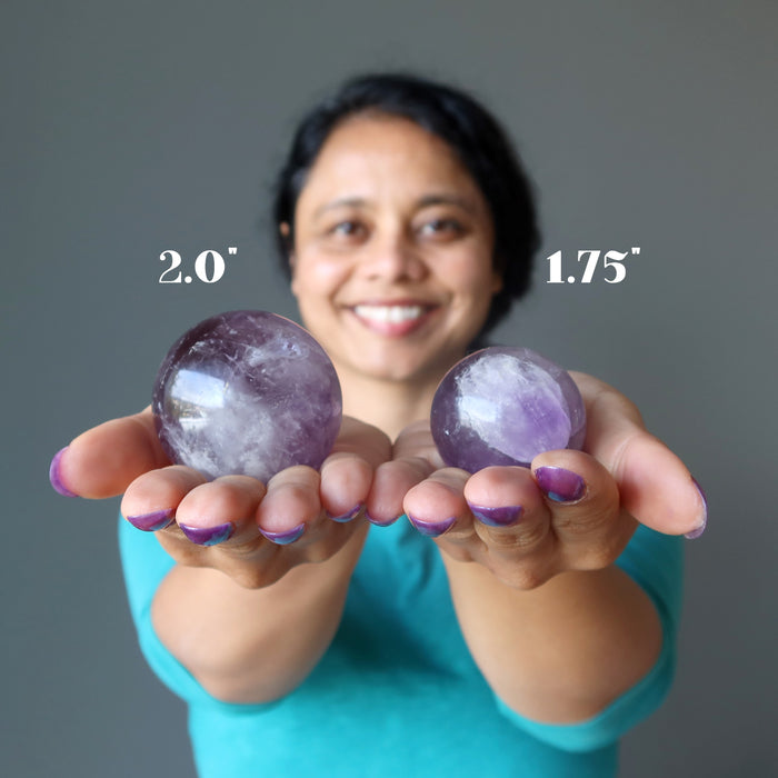 woman holding two amethyst spheres to show size difference