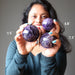sheila of satin crystals holding up three different sized amethyst spheres to show difference in size