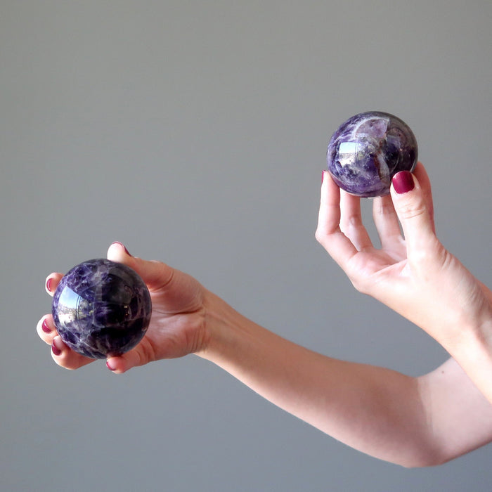 hands holding two dark purple amethyst spheres