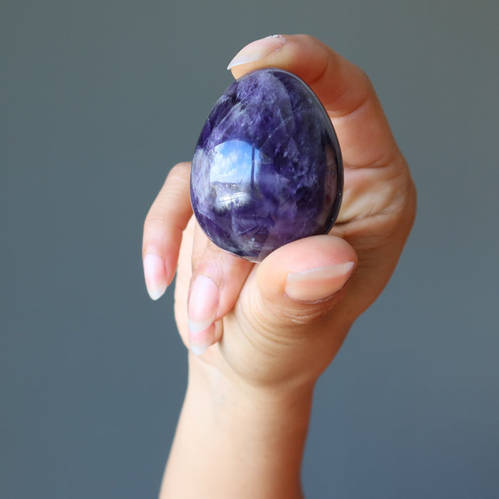 fingers holding dark purple amethyst gemstone egg