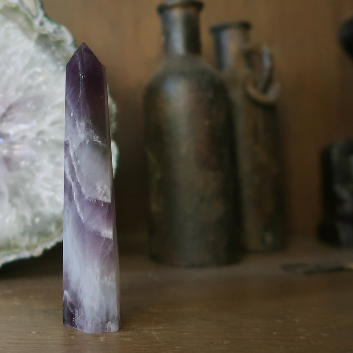 3.5-4 x 0.6 to 1 inches purple Amethyst Chevron crystal point tower Wand with other crystal and antigue bottle in the background