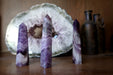 a set of three of 3.5-4 x 0.6 to 1 inches purple Amethyst Chevron crystal point tower Wands in front of  amethyst geode crystal and two antigue bottles in the background