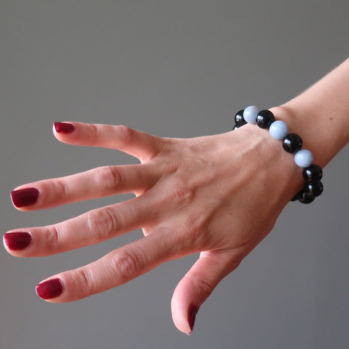 female hand modeling blue angelite and black rainbow obsidian stretch bracelet