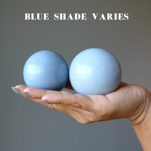 hand holding two angelite spheres showing blue shade varies
