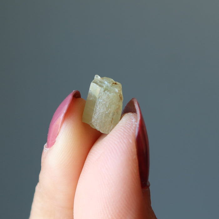 fingers holding a raw green apatite stone