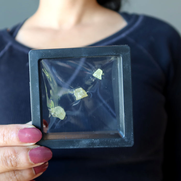 model holding three raw green apatite stones in a transparent case