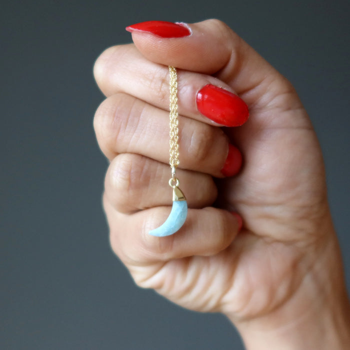 hand holding aquamarine crescent moon pendant on gold necklace