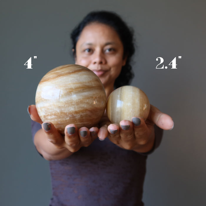 sheila of satin crystals holding up two aragonite spheres to show 4" and 2.4" sizes