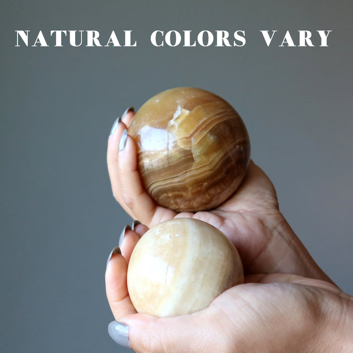 hands holding two aragonite spheres to show natural colors vary