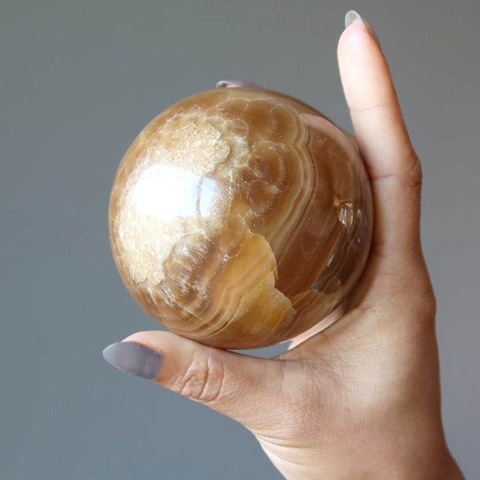 brown aragonite sphere in hand