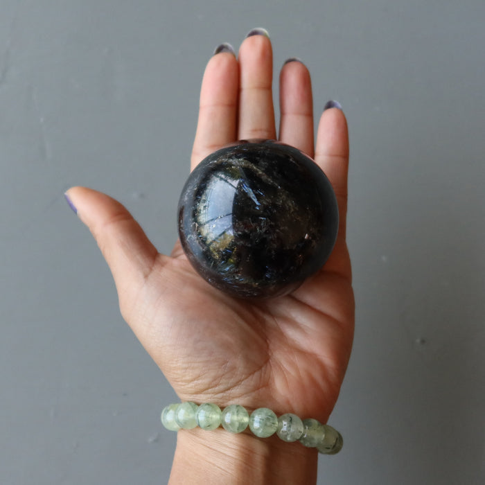 hand wearing prehnite bracelet holding arfvedsonite sphere in the palm