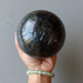 hand wearing prehnite bracelet holding large arfvedsonite sphere in the palm