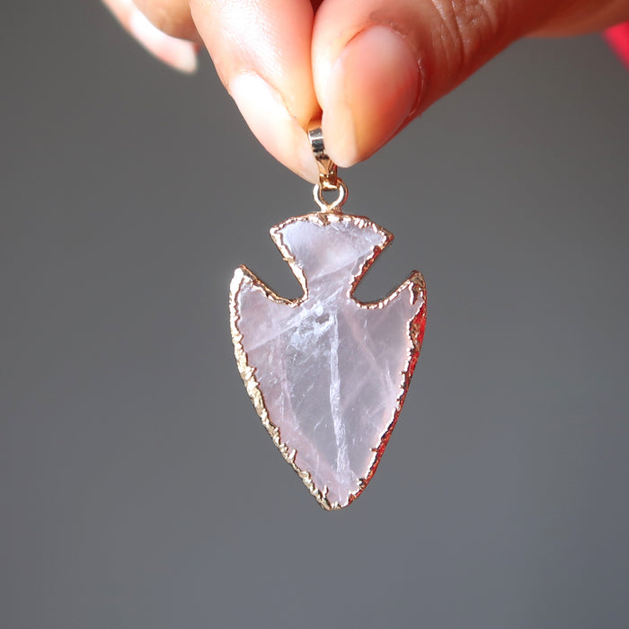 hand holding a rose quartz arrowhead pendant