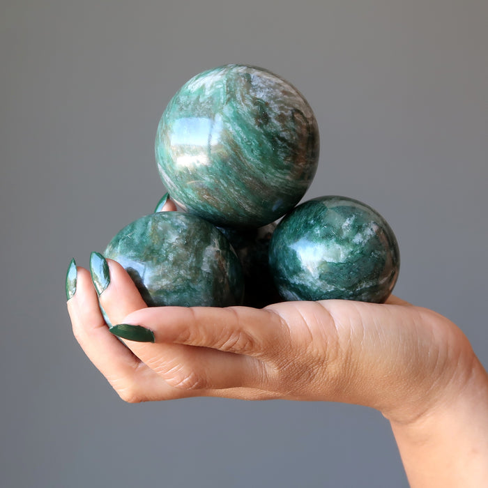 hand holding a pile of green and white streaked aventurine spheres