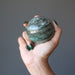 female hand holding up a green and white streaked aventurine sphere