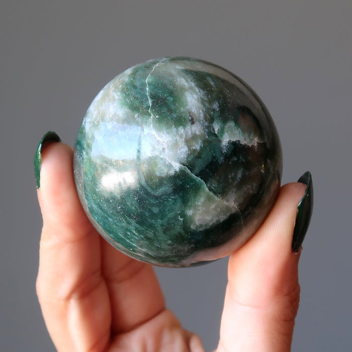 hand holding green and white streaked aventurine sphere