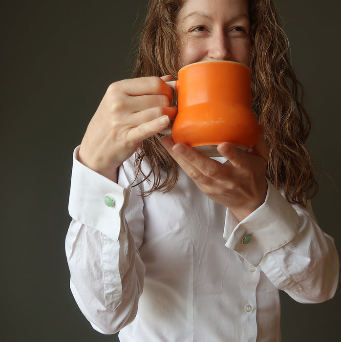 woman wearing white shirt with green cufflinks holding an orange coffee mug