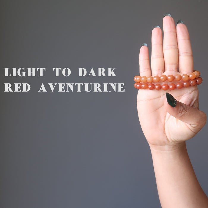 hand holding up two orange red aventurine bracelets to show the color variation from light to dark