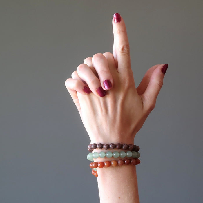 female hands pointing upwards modeling red, purple, green aventurine bracelet sets