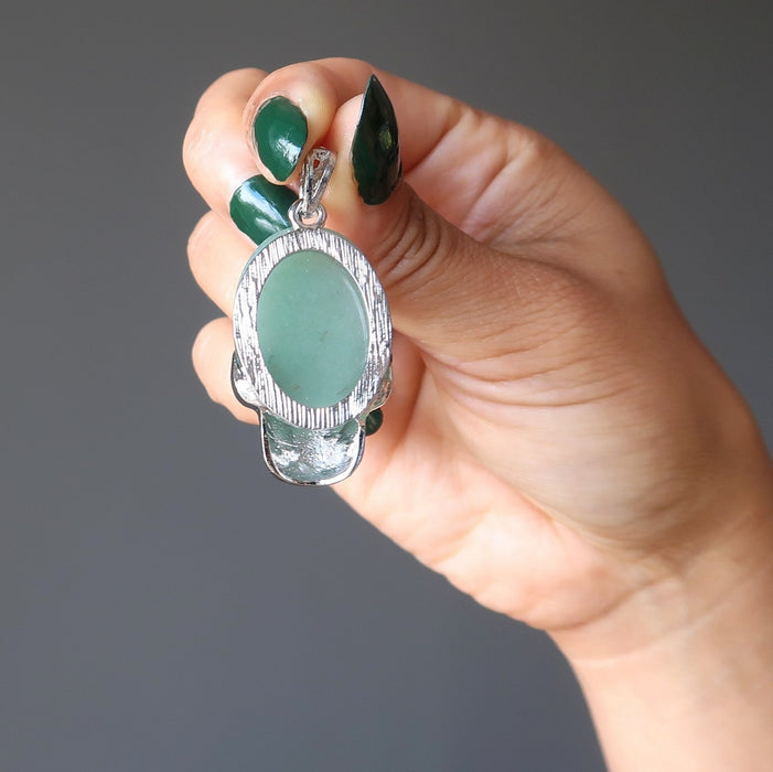 hand holding green aventurine in silver skull pendant showing backside