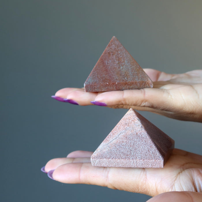 hands holding pink aventurine pyramids
