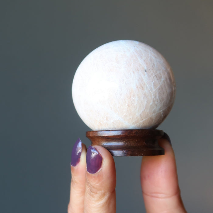 hand holding up a rosewood display stand with a cream moonstone ball