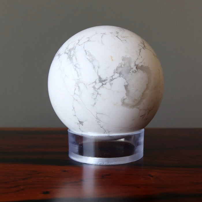 A  white and gray Howlite crystal ball is displaying on an acrylic stand.         