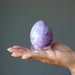 a palm holing a purple crystal egg on an acrylic stand.