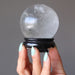 hand holding a clear quartz sphere on a black wood display stand