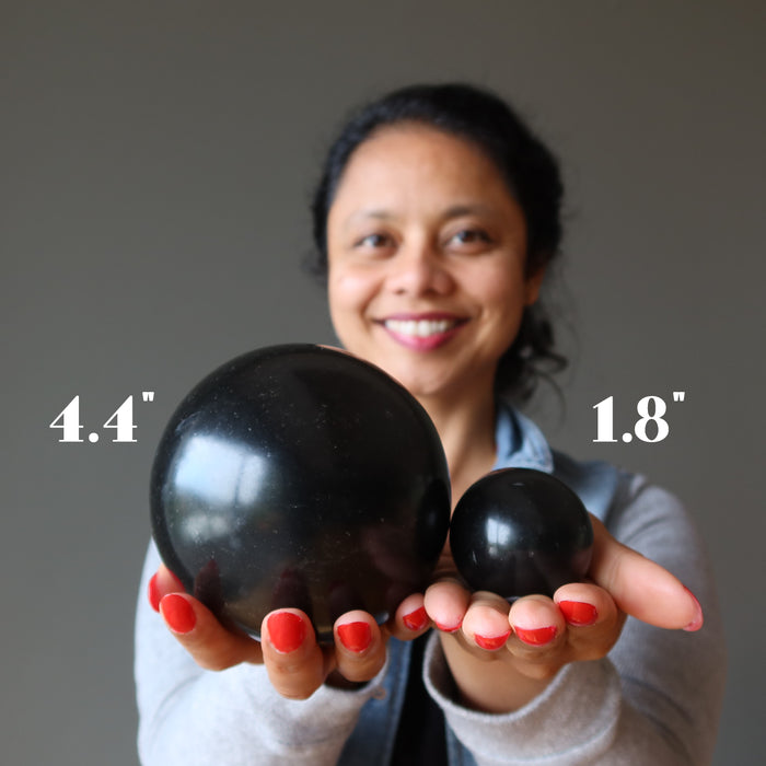 sheila of satin crystals holding 2 black basalt spheres to show size difference