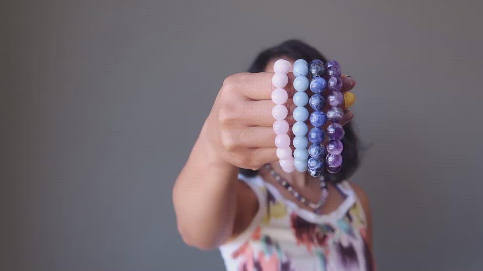 Sheila Satin holds the four Upper Chakra bracelets that she designs, and they include pink Rose Quartz, blue Angelite,, navy Sodalite, purple Amethyst