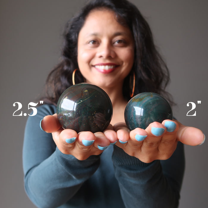 sheila of satin crystals holding two bloodstone spheres in her hands to show size difference