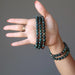female hand wearing and holding many faceted bloodstone bracelets