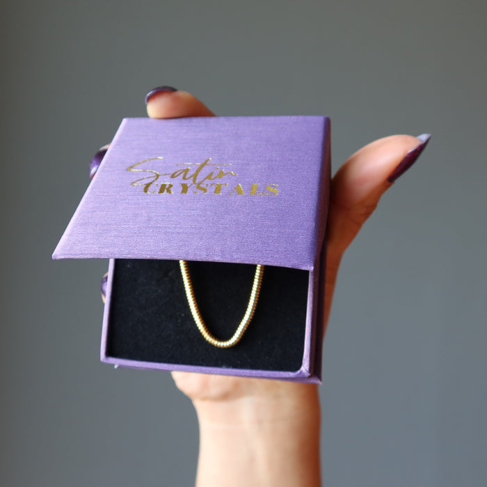 hand holding gold plated brass snake chain necklaces in purple gift box