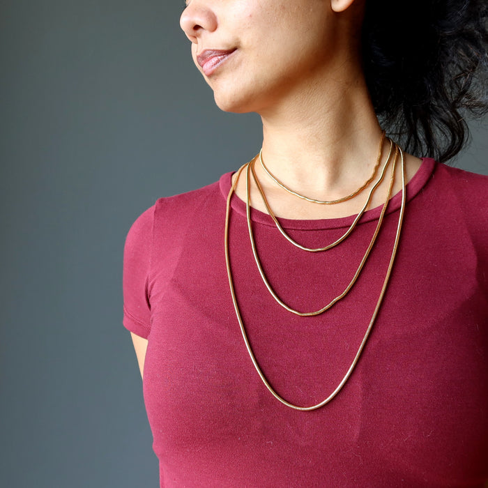 female model of satin crystals wearing 4 gold plated brass snake chain necklaces to show the different lengths