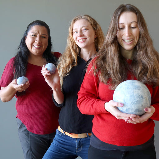 3 female models holding three different sizes of BLue Calcite sphere