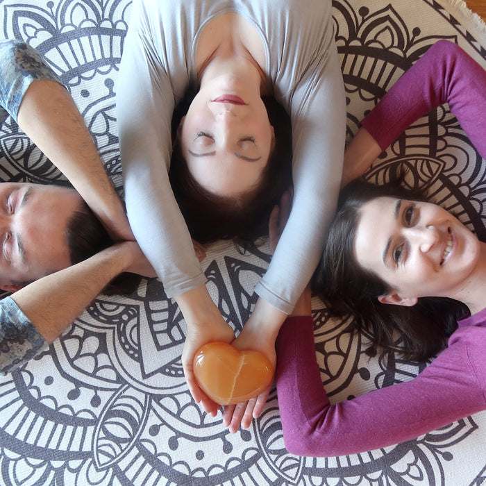 3 female models lying on the floor holding up their hands in the center with Golden Calcite Heart on one of their palms