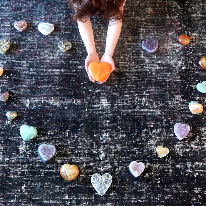 model holding Golden Calcite Heart sitting on the floor with many differrent crystal hearts forming heart shape on the floor