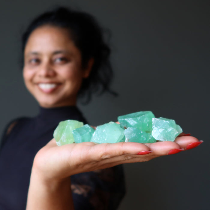 sheila of satin crystals holding a pile of waxy green calcite raw stones