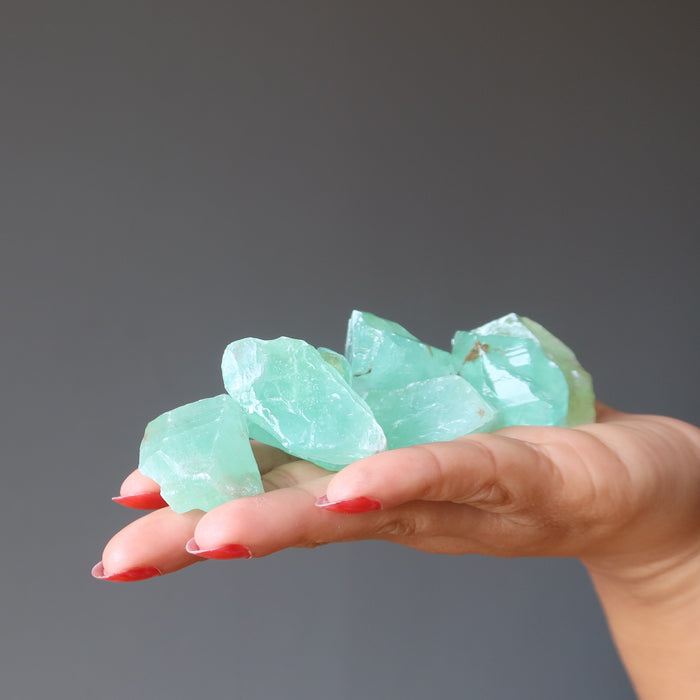 hand holding a pile of waxy green calcite raw stones